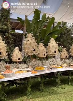 a table topped with lots of bird houses covered in grass and plants next to trees