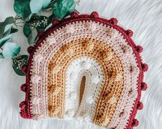 a crocheted pot holder with a rainbow shaped hole in the middle on a white rug