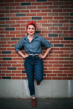 a woman leaning against a brick wall with her hands on her hips, wearing jeans and a denim shirt