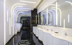 a long bathroom with sinks and mirrors on the walls, along with lights in the ceiling