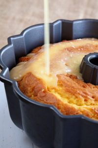 a bundt cake is being poured with icing from a black pan on a white table