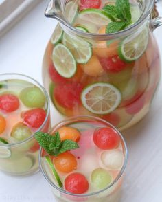 a jar filled with watermelon, lemon and grapefruit next to two glasses