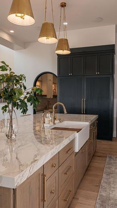 a large kitchen with marble counter tops and gold fixtures on the island, along with two hanging lights