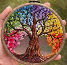 a person holding up a colorful painted tree on a piece of wood in their hand