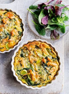 two pies sitting on top of a wooden table next to a plate with greens