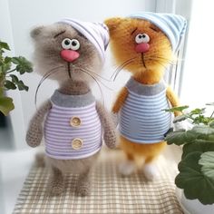 two stuffed animals dressed in sweaters and hats on a table next to a potted plant