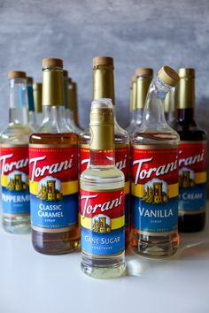 four bottles of torani syrup are lined up on a table with one bottle in the foreground