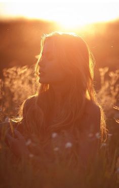 a woman standing in a field with the sun shining down on her face and long hair