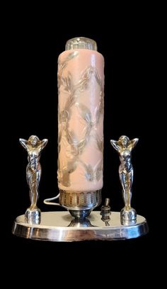 a pink candle sitting on top of a table next to two silver figurines