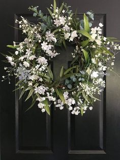 a wreath with white flowers and greenery hangs on a black front door in the daytime