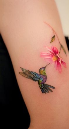 a hummingbird and flower tattoo on the back of a woman's left shoulder