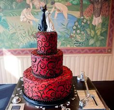 a three tiered red cake sitting on top of a metal tray with an artistic painting behind it