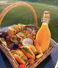 a picnic basket filled with sandwiches, cheese and fruit next to a bottle of orange juice