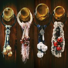 four pieces of jewelry hanging from hooks on a wooden wall with beads and bells attached to them