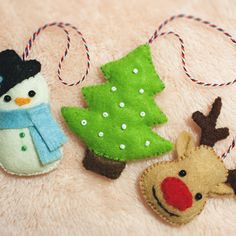 three felt christmas ornaments are sitting on a pink surface, one is a snowman and the other is a reindeer