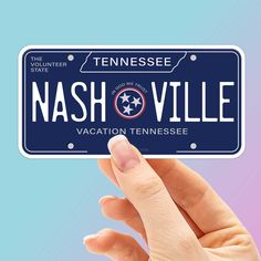 a hand holding up a license plate for nashville, tennessee on a blue and pink background