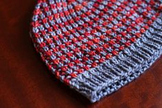 a close up of a knitted tie on a wooden table with red and gray colors