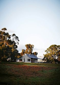 a white house sitting in the middle of a lush green field with trees around it