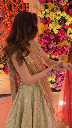 two women in dresses standing next to each other with flowers on the wall behind them