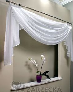 a white curtain is hanging over a mirror in a bathroom with flowers on the ledge