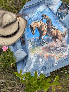 a cowboy hat and jean jacket laying on the ground next to some wildflowers