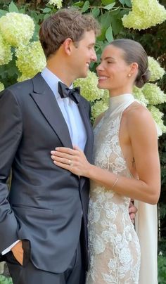 a man and woman in formal wear standing next to each other with flowers behind them