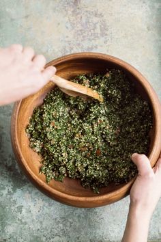 a person is mixing herbs in a wooden bowl