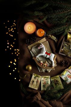 a table topped with cards and candles next to a christmas tree covered in lights on top of a brown cloth