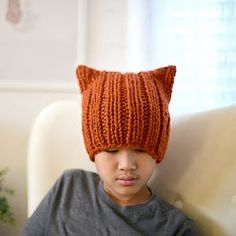 a young boy wearing an orange knitted cat ear hat sitting on a white couch