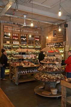 people are standing around in a store with shelves full of food and wine bottles on the wall