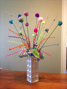 a white vase filled with lots of colorful streamers on top of a wooden table