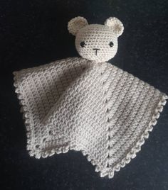 a crocheted teddy bear laying on top of a black table next to a white blanket