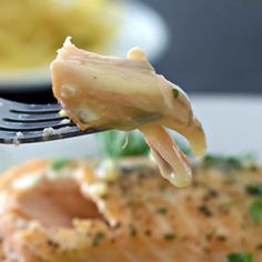 a piece of fish being lifted from a fork with some sauce on it and another dish in the background