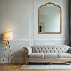 a living room with a couch, mirror and lamp on the wall next to it