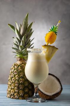 a pineapple drink in a tall glass next to a half - eaten pineapple