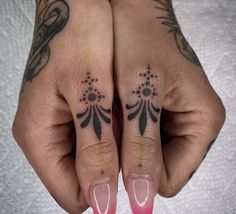 two hands with tattoos on their fingers and one holding a pink manicured nail