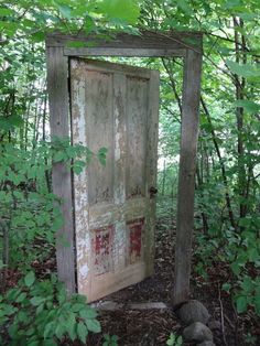 an old outhouse in the woods surrounded by green leaves and rocks, with its door open