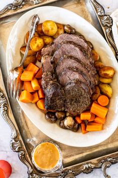 a white plate topped with meat, potatoes and carrots next to an orange sauce