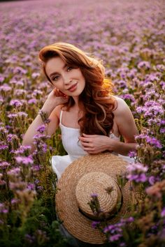 a woman in a field with purple flowers and a straw hat on her head, smiling at the camera