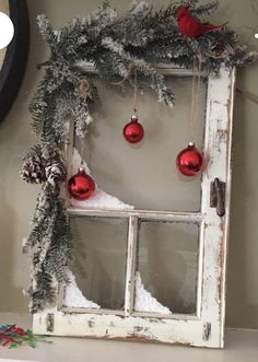 an old window decorated for christmas with ornaments hanging from the frame and snow on the windowsill