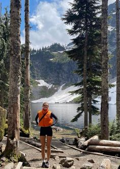 a woman in an orange vest is standing on rocks near some trees and looking at the camera