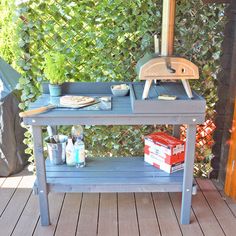 an outdoor grill on a wooden deck next to a green fence and shrubbery behind it