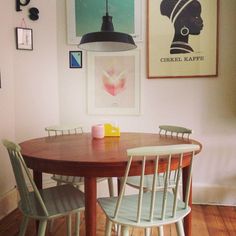 a dining room table with four chairs and two pictures on the wall above it,