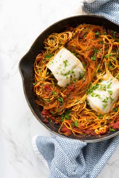 fish and noodles in a skillet with parsley on the side for garnish