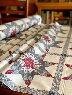 a quilted table runner with red and white snowflakes on it, sitting next to a bookcase