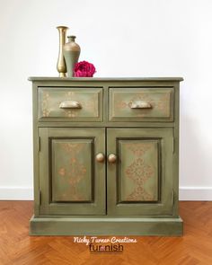 a green cabinet with two vases on top of it and a pink flower in the middle