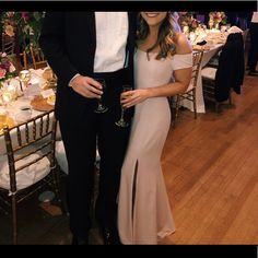 a man and woman standing next to each other at a dinner table with wine glasses in their hands