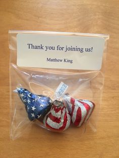 two small american flags in plastic bags on a table with a thank you for joining us sign