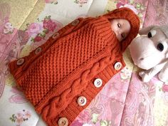 a baby laying on top of a bed next to a stuffed animal and wearing an orange sweater