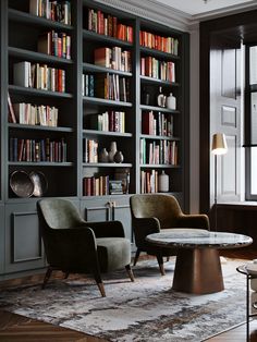 two chairs and a table in front of a bookcase with many books on it